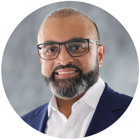 Smiling man with glasses, a beard, and mustache, wearing a white dress shirt and navy blue blazer, posed against a gray background.